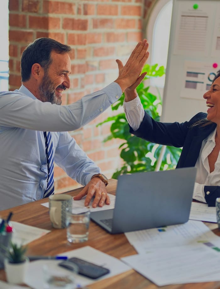 Two colleagues high-fiving across a meeting table